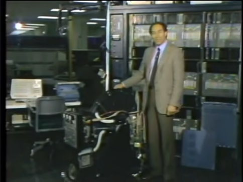 A man in a suit standing in front of a large, 1950s-era hard disk unit, which comes up to his waist.